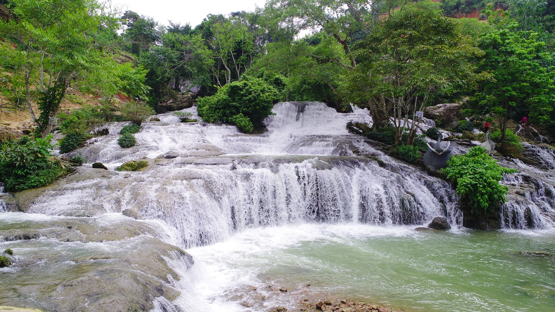 The waterfall flows in the heart of the cool green forest.